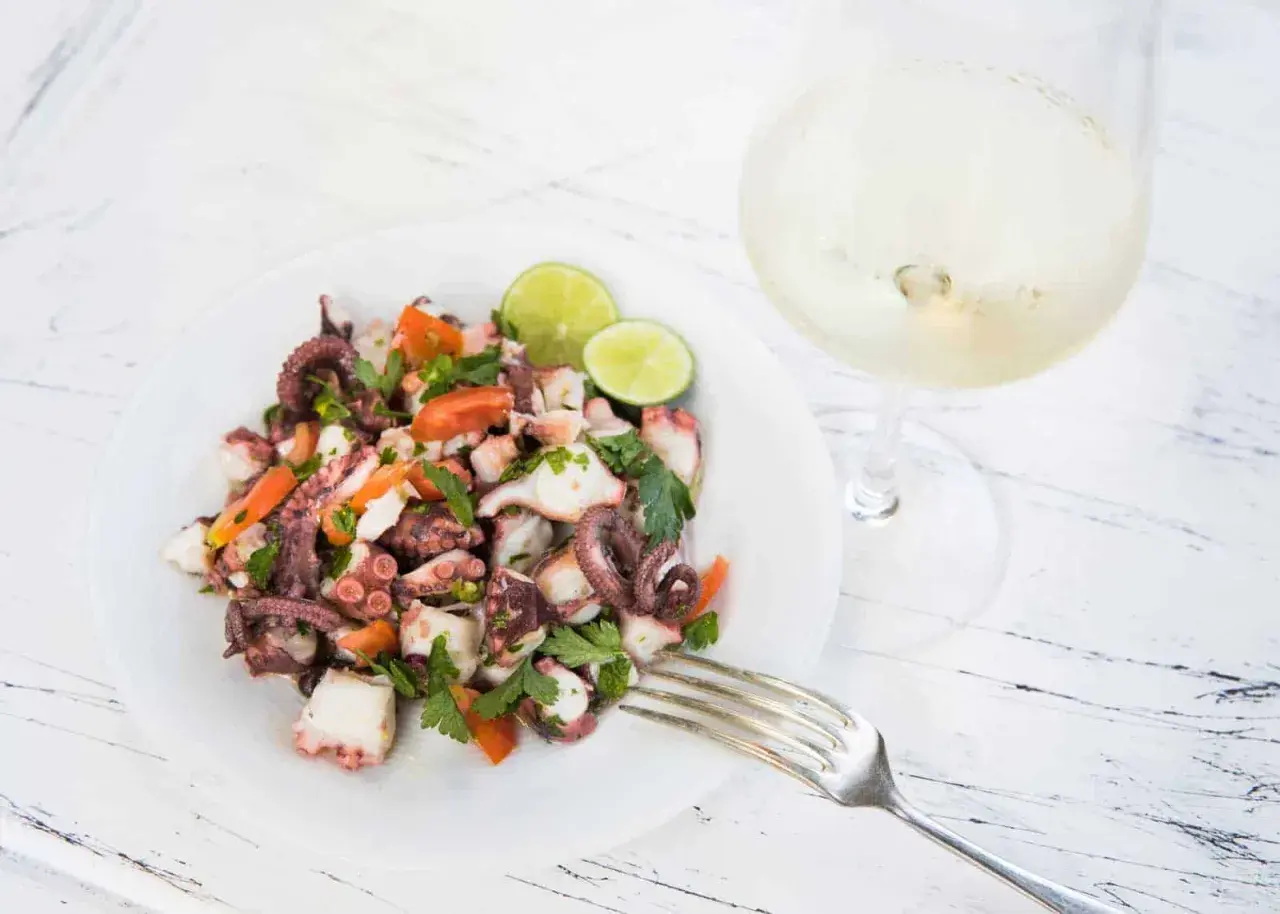 Frischer oktopus salat mit Tomaten, Petersilie und Limette, daneben ein Glas Weißwein.