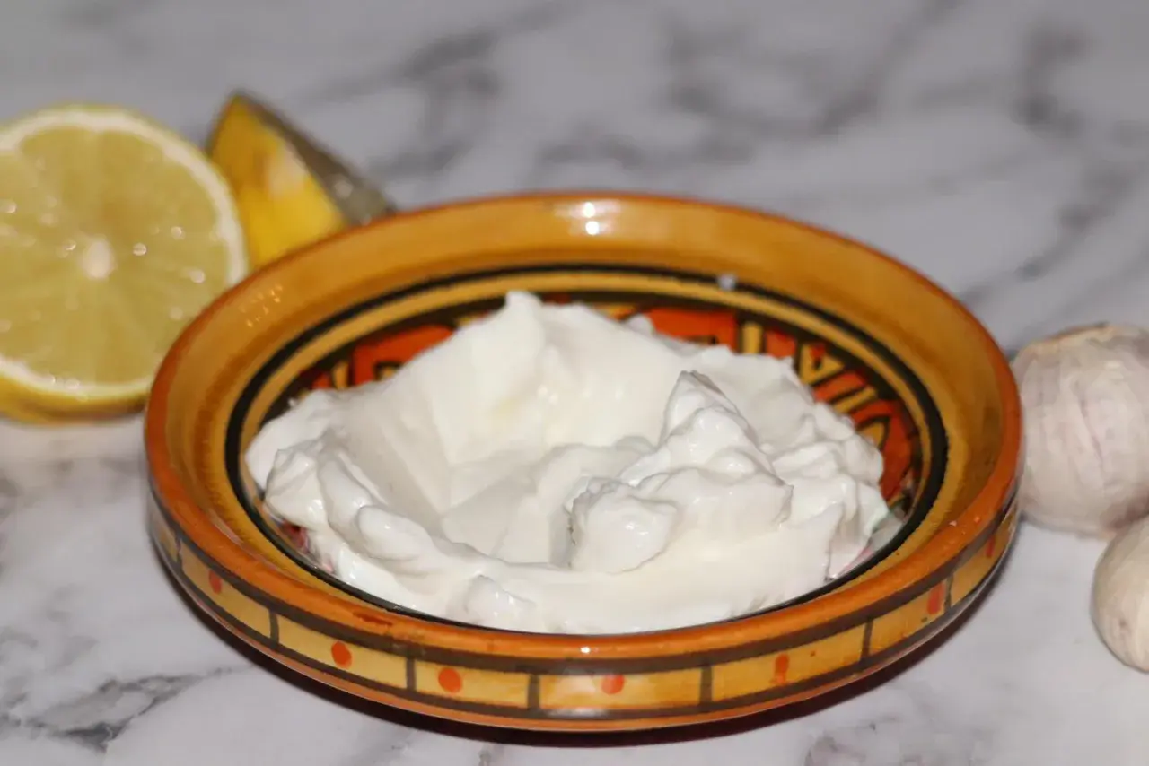 Krämig vitlökssås, perfekt för ditt toum recept. Citron och vitlök bredvid skålen.