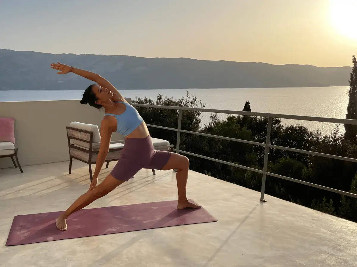 Mujer en postura de yoga en terraza con vista al mar al atardecer. Un momento de **slow life** y conexión.