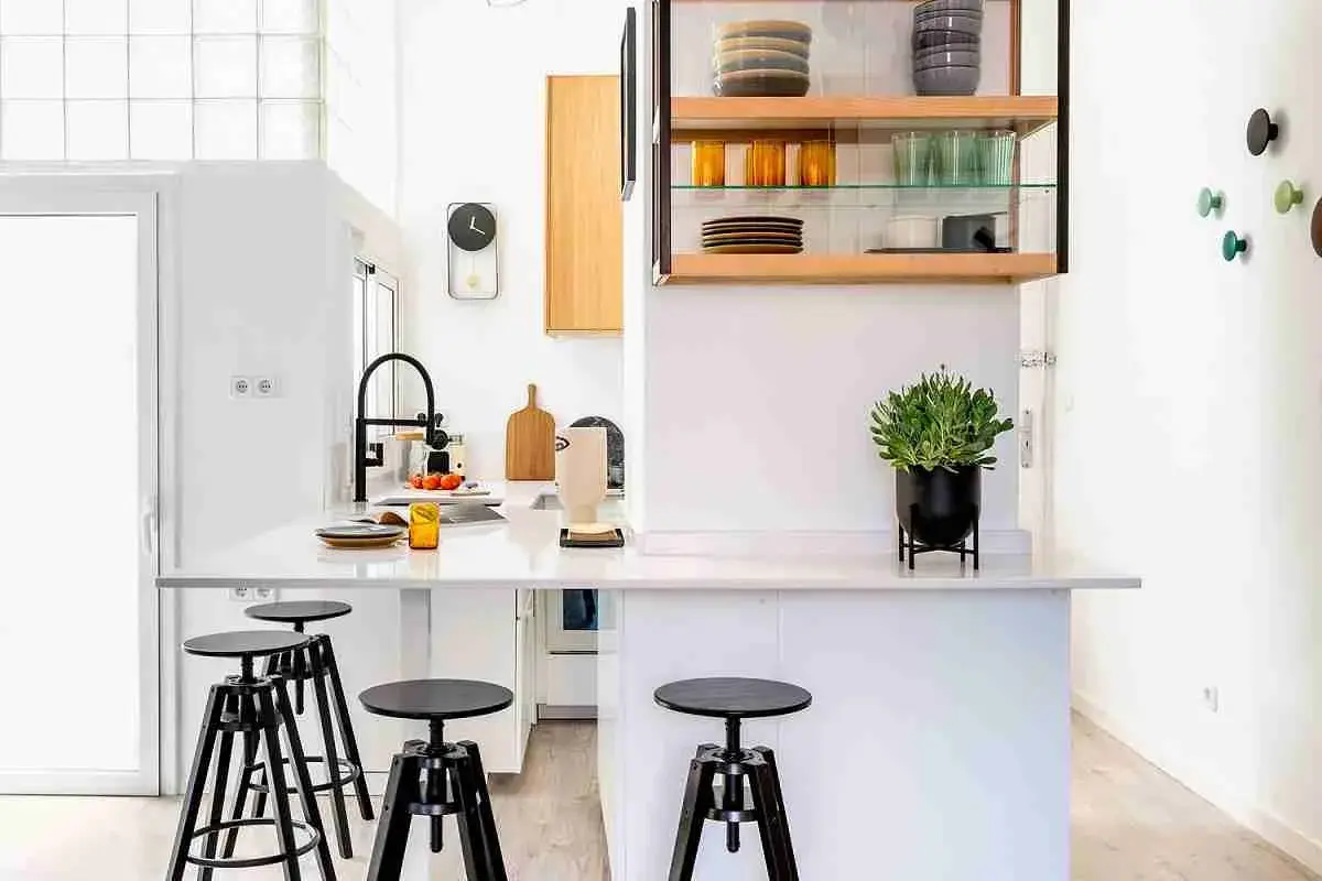 Cocinas sin muebles altos, con una isla central, taburetes negros y estanterías abiertas con vajilla.