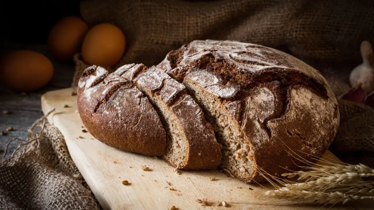 Pane di segale affettato su tagliere, con uova e spighe. Attenzione, il pane di segale fa ingrassare se consumato in eccesso.