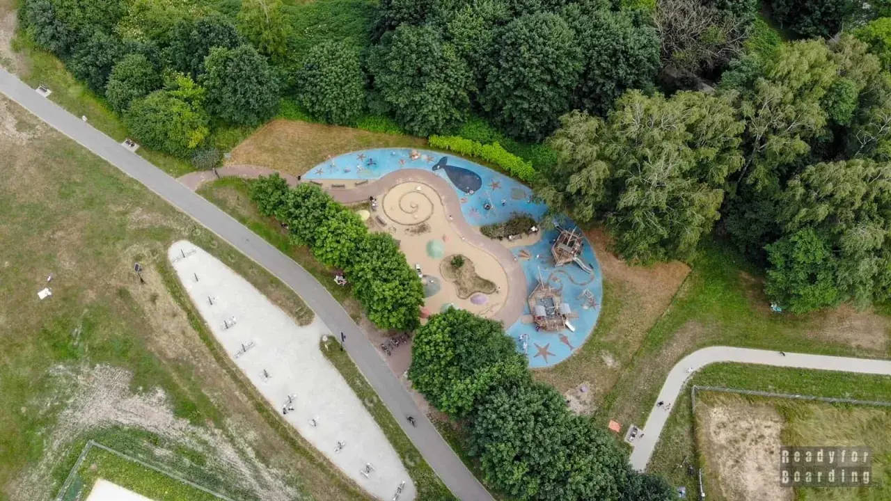 Kolorowy plac zabaw w kształcie fali z wielorybem i statkami pirackimi, otoczony zielenią. Idealne miejsce na zabawę dla dzieci w Łodzi.