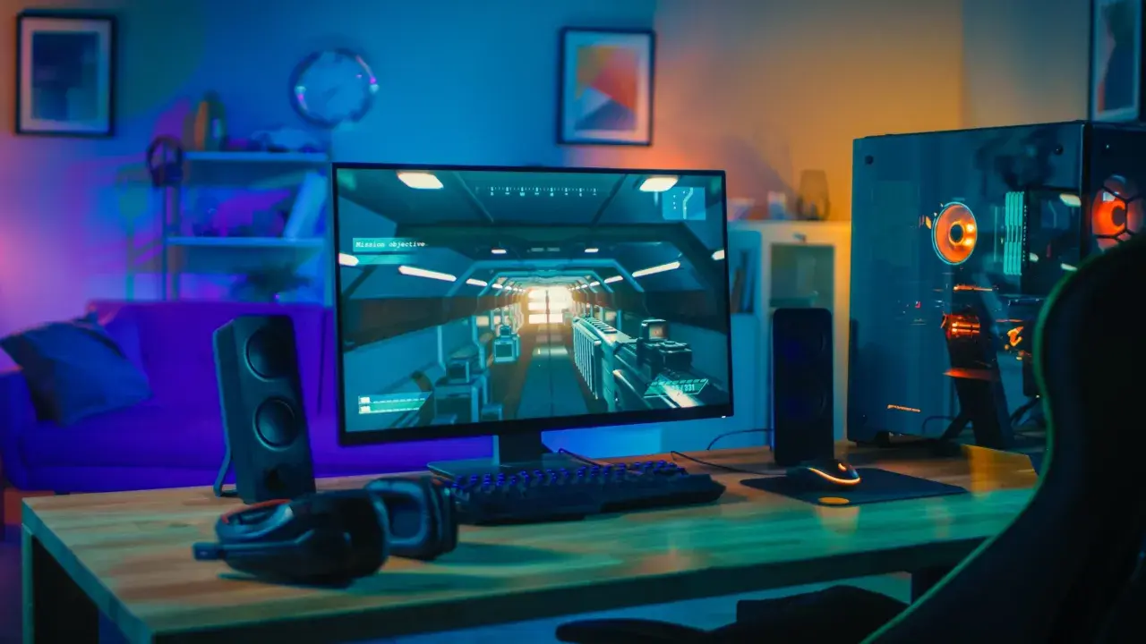 Bureau de jeu avec PC puissant, écran affichant un jeu vidéo, clavier, souris et casque. Ambiance lumineuse, parfait pour config windows 11.