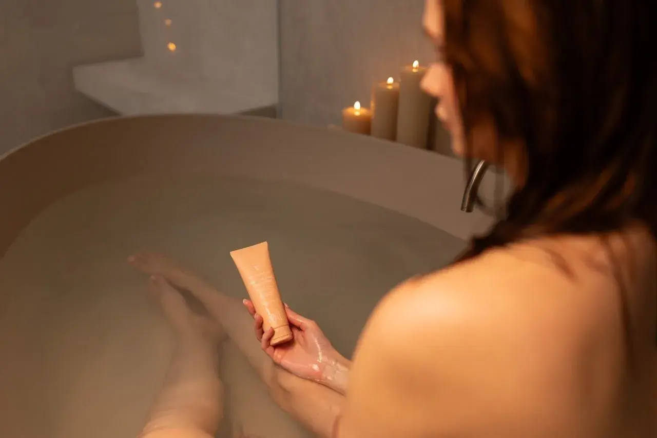 En kvinna håller en tub med kräm i ett bad. Doften av klorin på huden kan lindras med denna fuktgivande produkt.