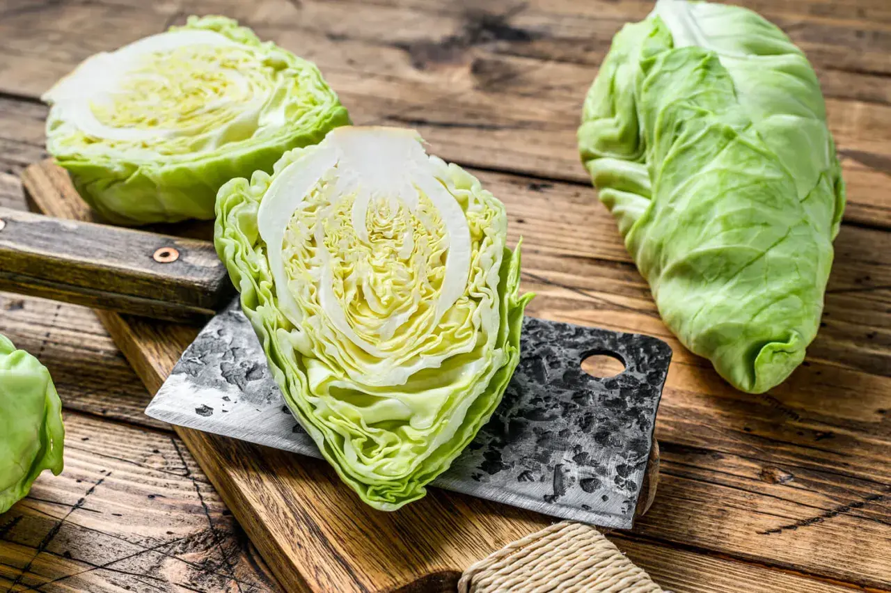 Frischer Spitzkohl, halbiert und auf einem Holzbrett mit einem Hackmesser. Perfekt, um Spitzkohl roh zu essen für einen knackigen Salat.