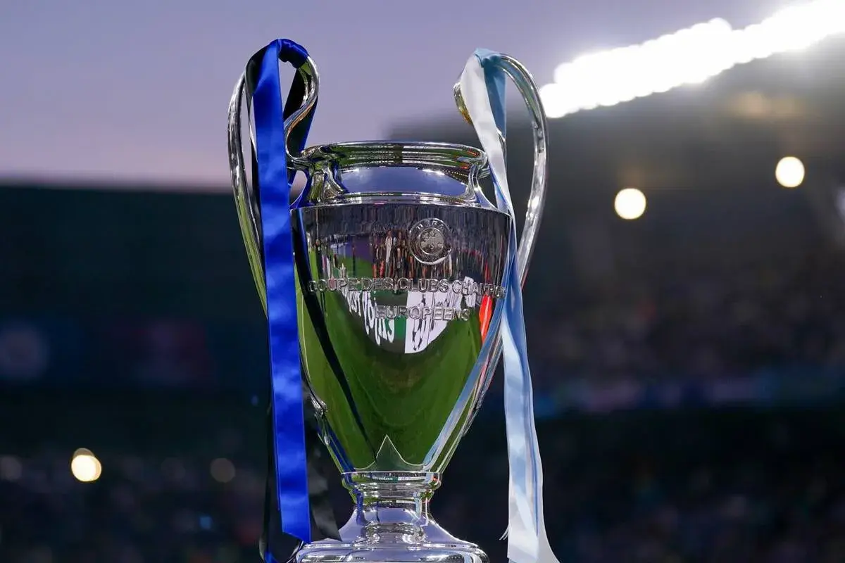 Trofeum Ligi Mistrzów, symbol marzeń i celów w piłkarskich rankingach. Błyszczący puchar z niebieskimi i jasnymi wstążkami, odbijający światła stadionu.