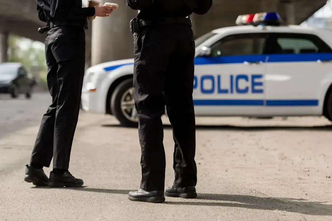 Policjanci w pełnym umundurowaniu stoją obok radiowozu. Ich wyposażenie jest gotowe do akcji.
