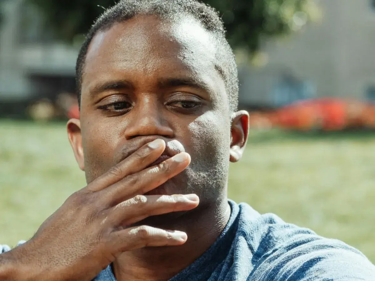 Uomo con mano sulla bocca, pensieroso. Il gesto di coprirsi la bocca può avere un **sputare significato psicologico** di repressione o riflessione interiore.