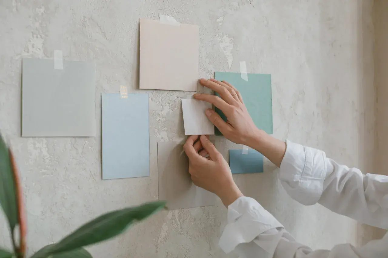Händer arrangerar färgglada papper på en vägg. Tre tavlor bredvid varandra bildar en del av en moodboard.