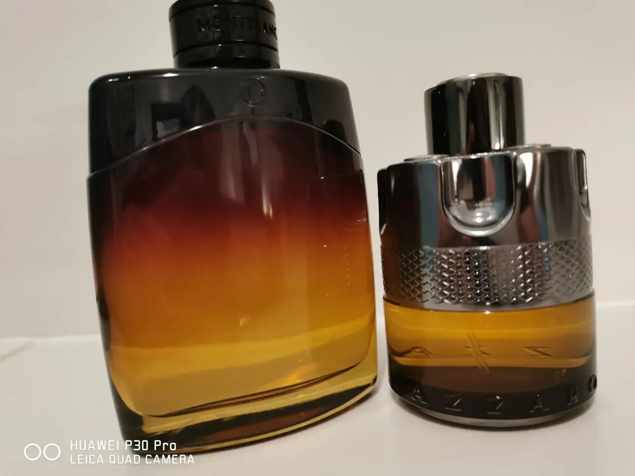 Dwa flakony perfum: jeden z gradientem od czerni do bursztynu, drugi z metalicznym wykończeniem i napisem AZZARO. Idealne na noc.