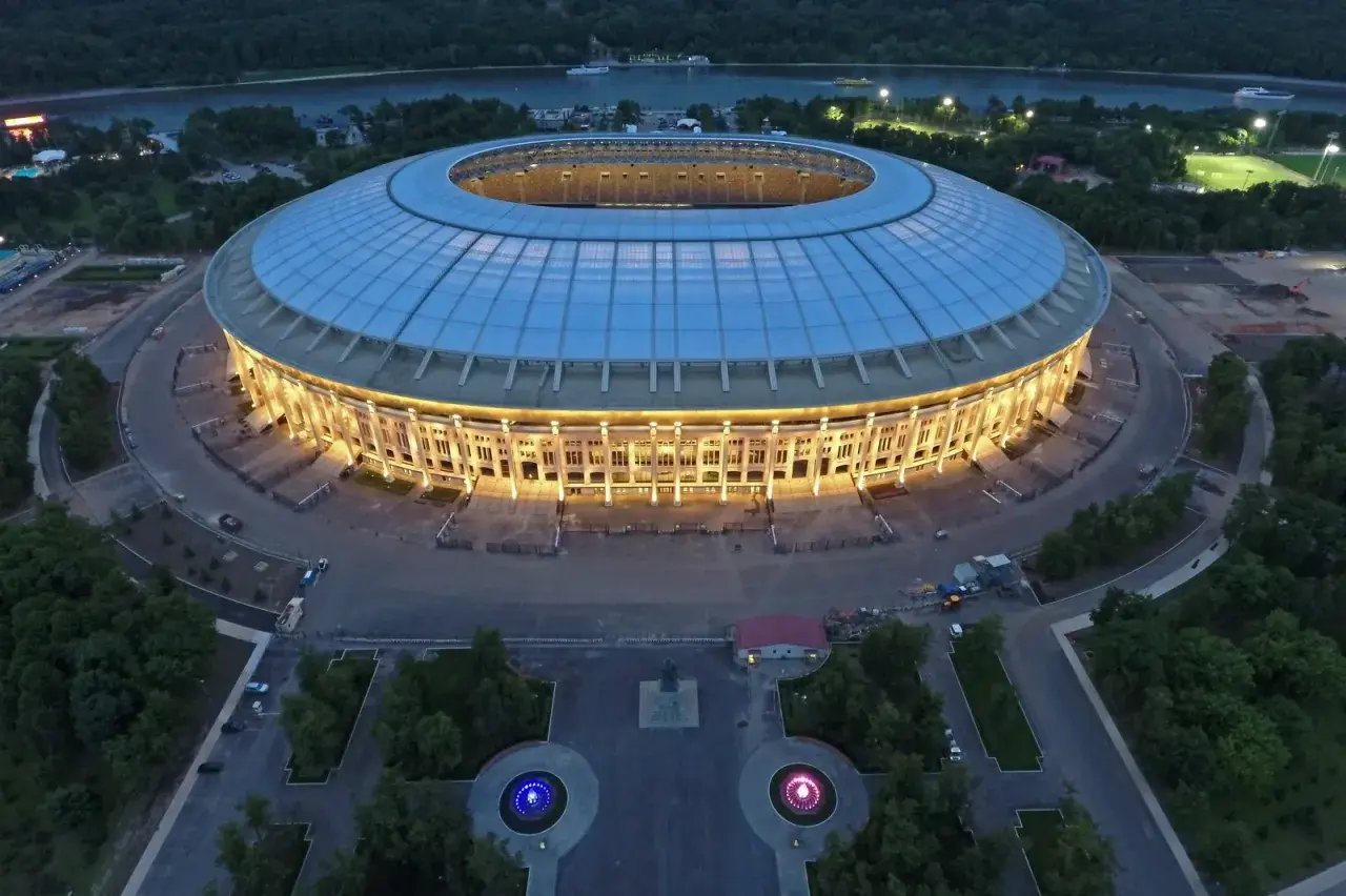 Oświetlony moskiewski stadion w nocy, z widokiem na rzekę i otaczający go las.
