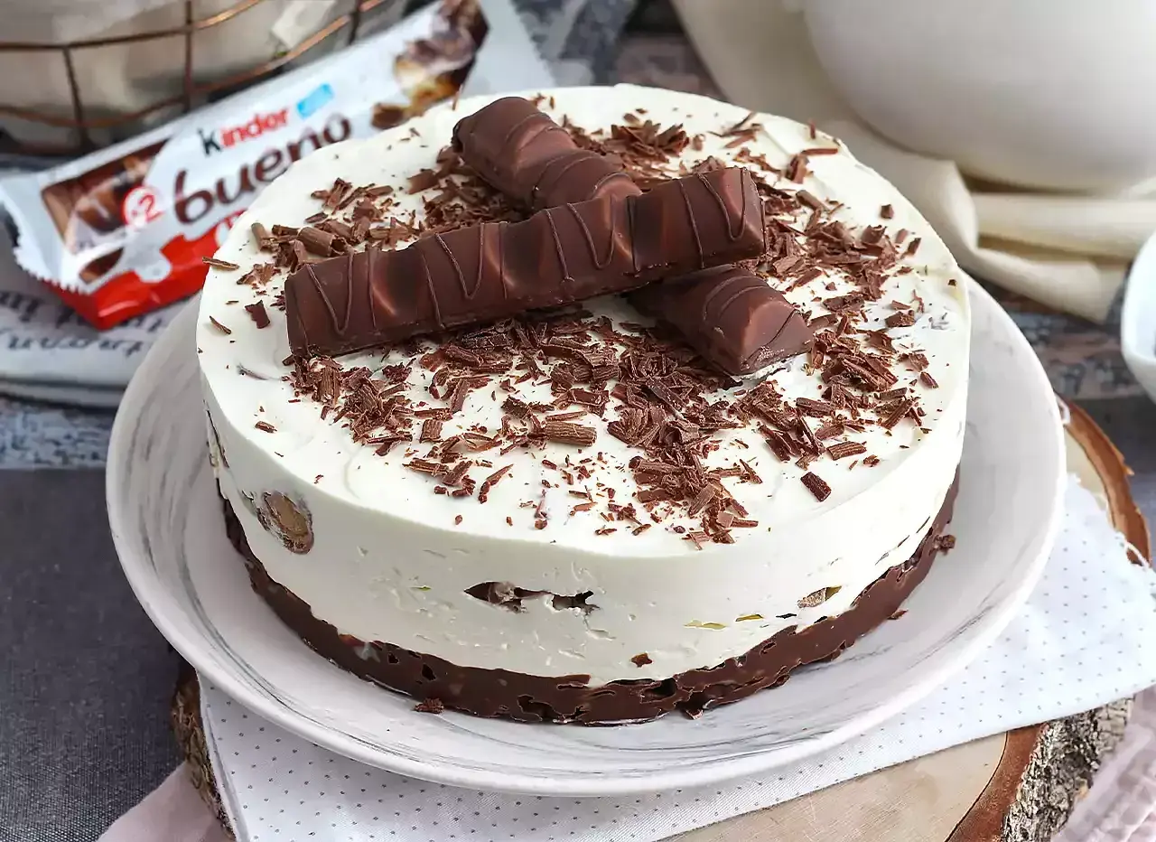Pyszna tarta Kinder Bueno z kremem i czekoladowymi wiórkami, ozdobiona batonikami.