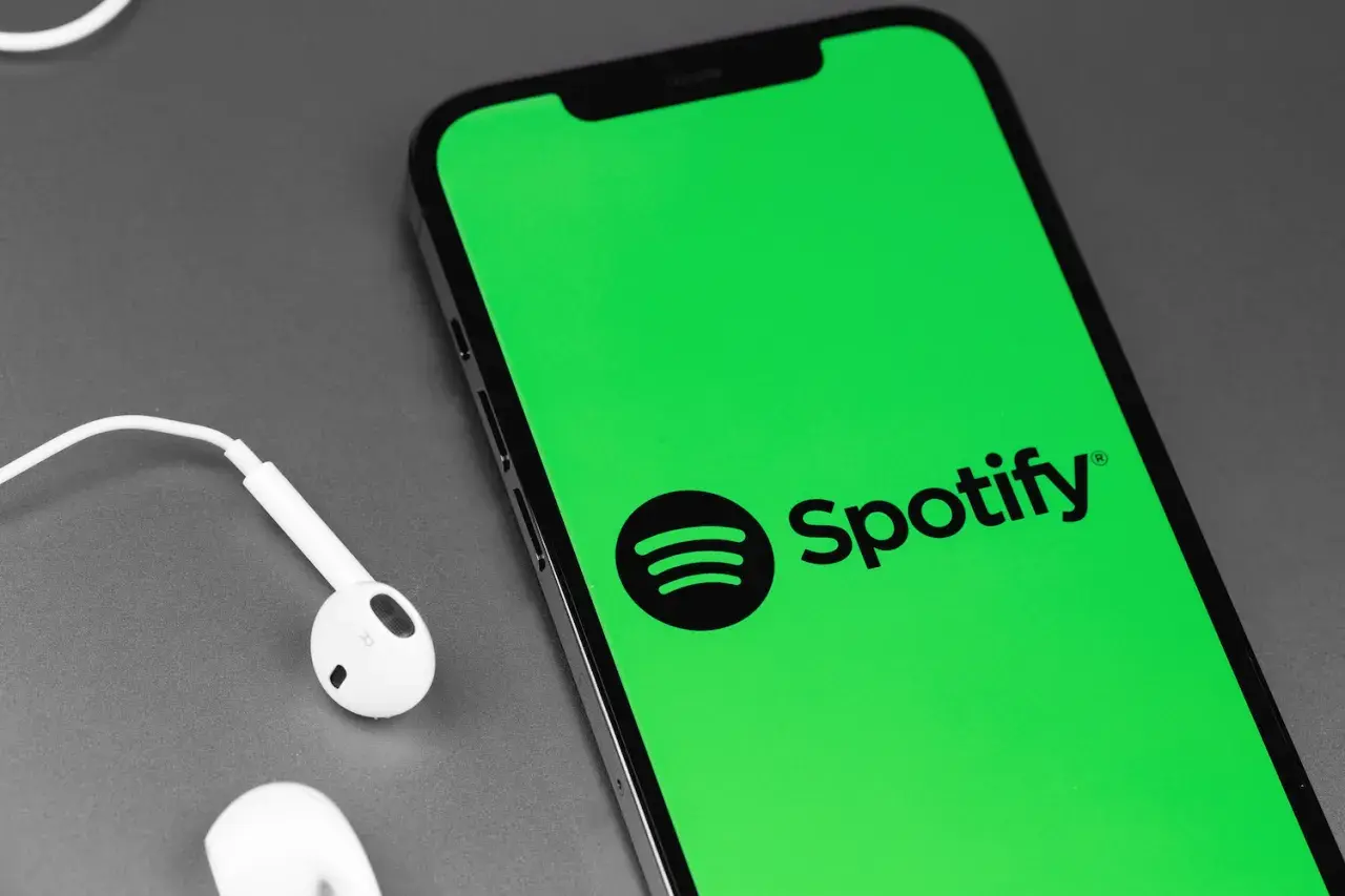 Telefon z zielonym ekranem i logo Spotify, obok białe słuchawki. Słuchaj muzyki za darmo dzięki Spotify free.