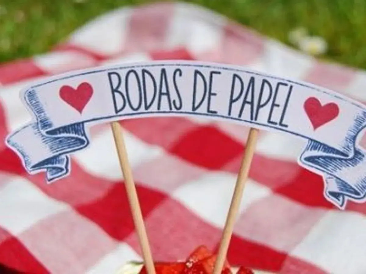 Un letrero de "Bodas de Papel" con corazones rojos, sobre un mantel de cuadros rojos y blancos.