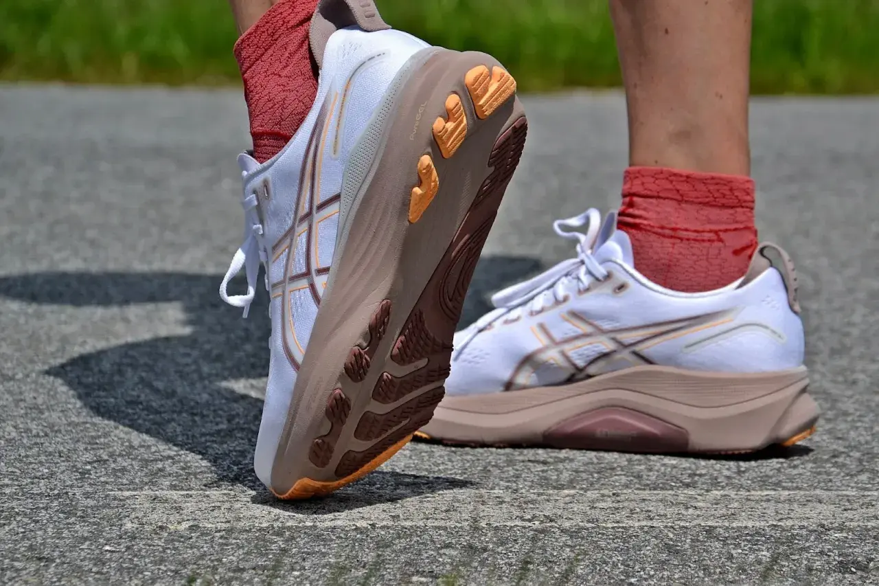 Białe buty do biegania Asics z pomarańczowymi akcentami na podeszwie. Firma Asics słynie z innowacyjnych rozwiązań.