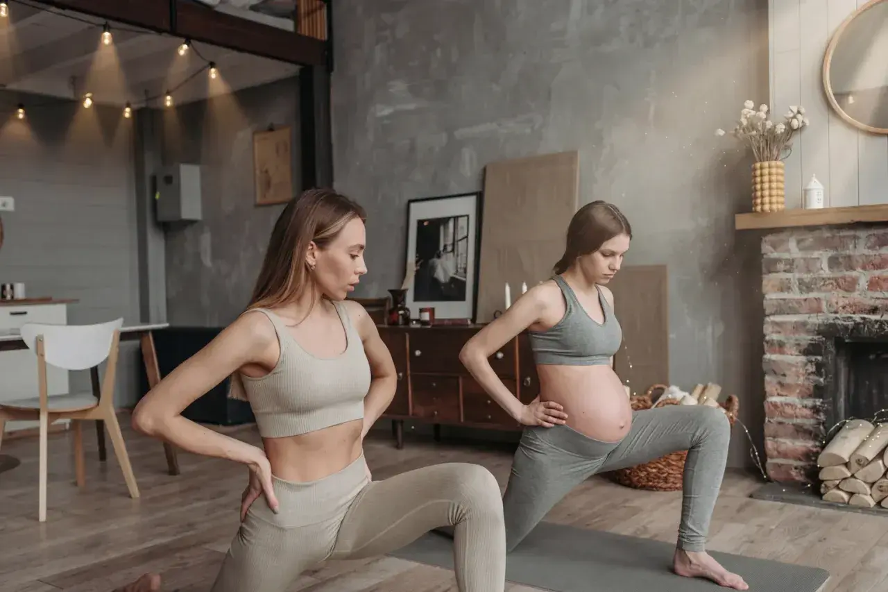 Två kvinnor gör yoga gravid i ett mysigt rum. Den ena kvinnan är gravid och den andra är hennes träningskompis.