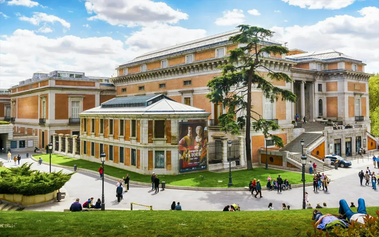 Muzeum Prado w Madrycie z ludźmi odpoczywającymi na trawie i zwiedzającymi.
