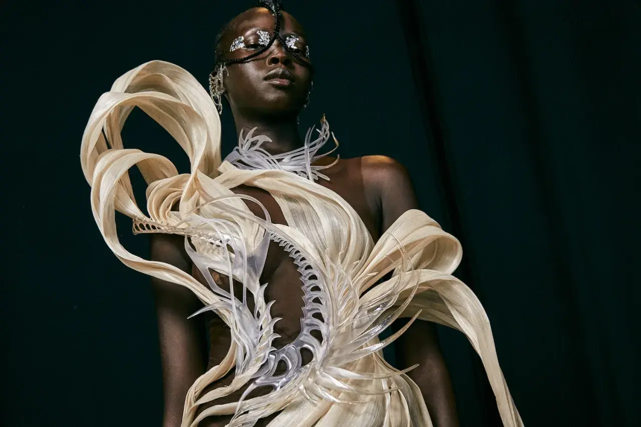 Mannequin portant une création avant-gardiste, un vêtement d'impression 3D aux formes organiques et futuristes, orné de détails argentés sur le visage.