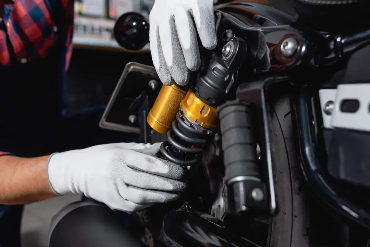 Mains gantées ajustant un amortisseur doré sur une moto. Faut-il changer les 4 amortisseurs pour une meilleure tenue de route ?