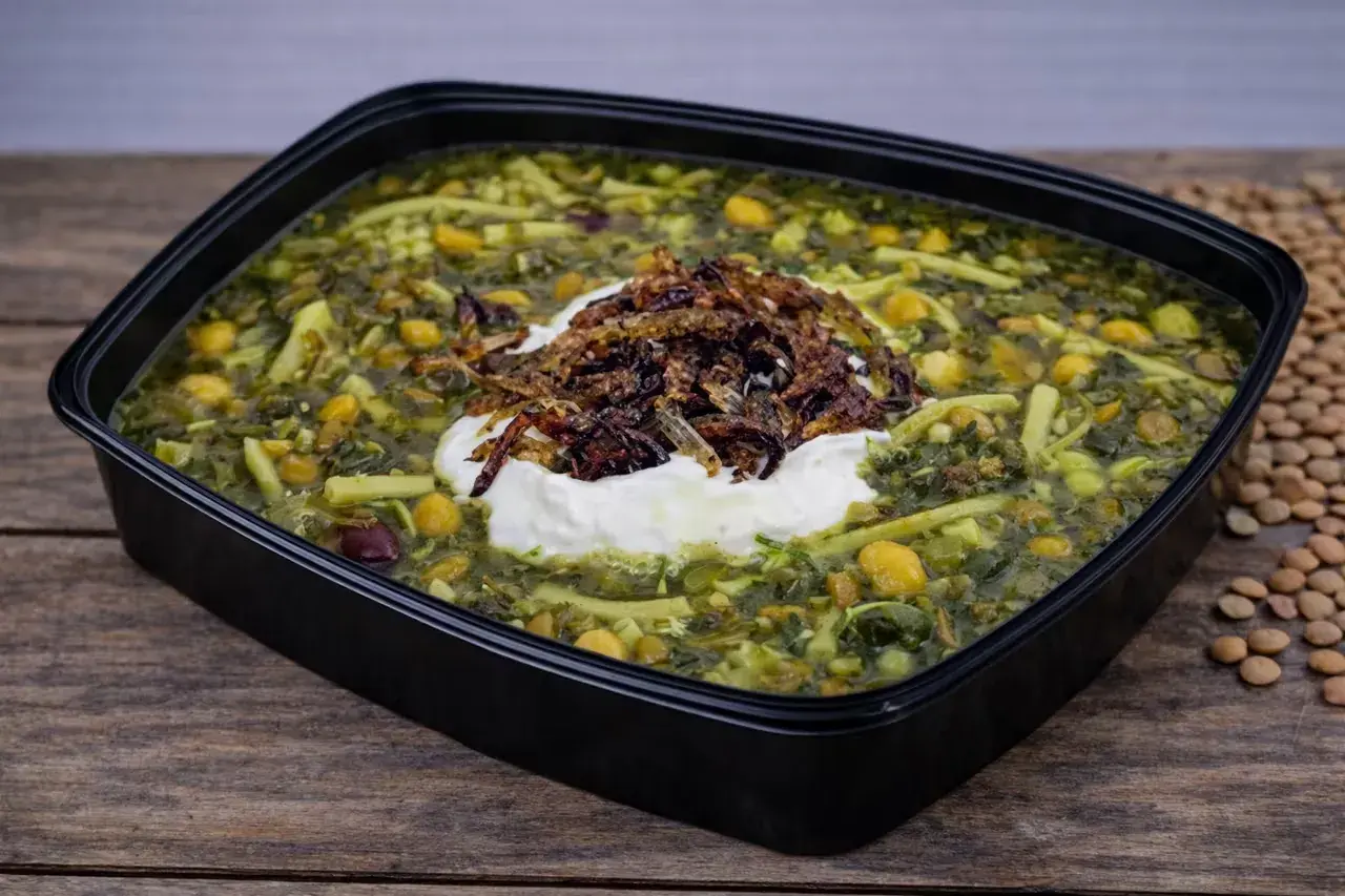 En skål med grön ash reshteh, en persisk örtsoppa med nudlar, kikärtor och linser, toppad med yoghurt och friterad lök.