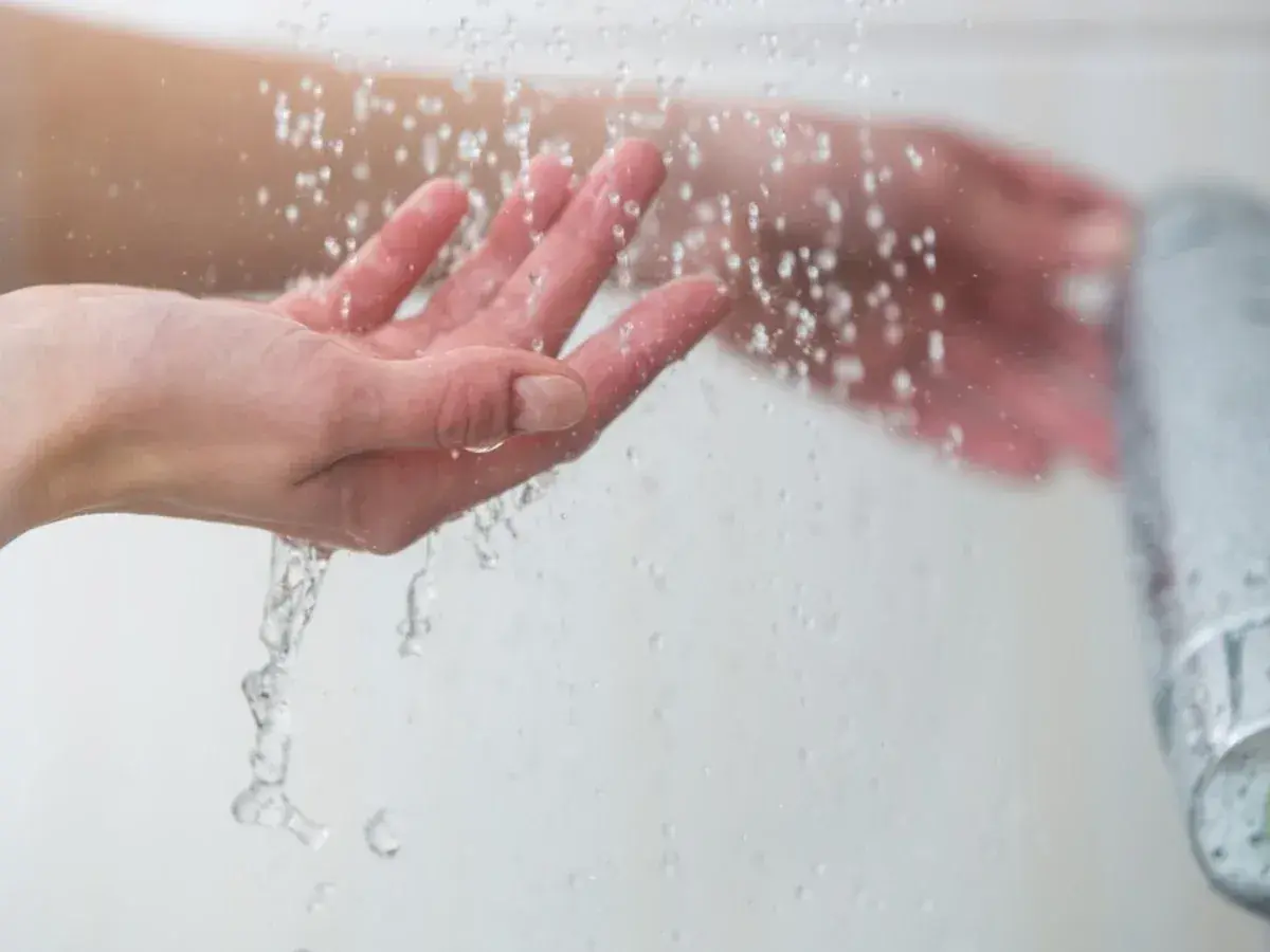 Manos bajo un chorro de agua fría, sintiendo el frescor al ducharse con agua fría.