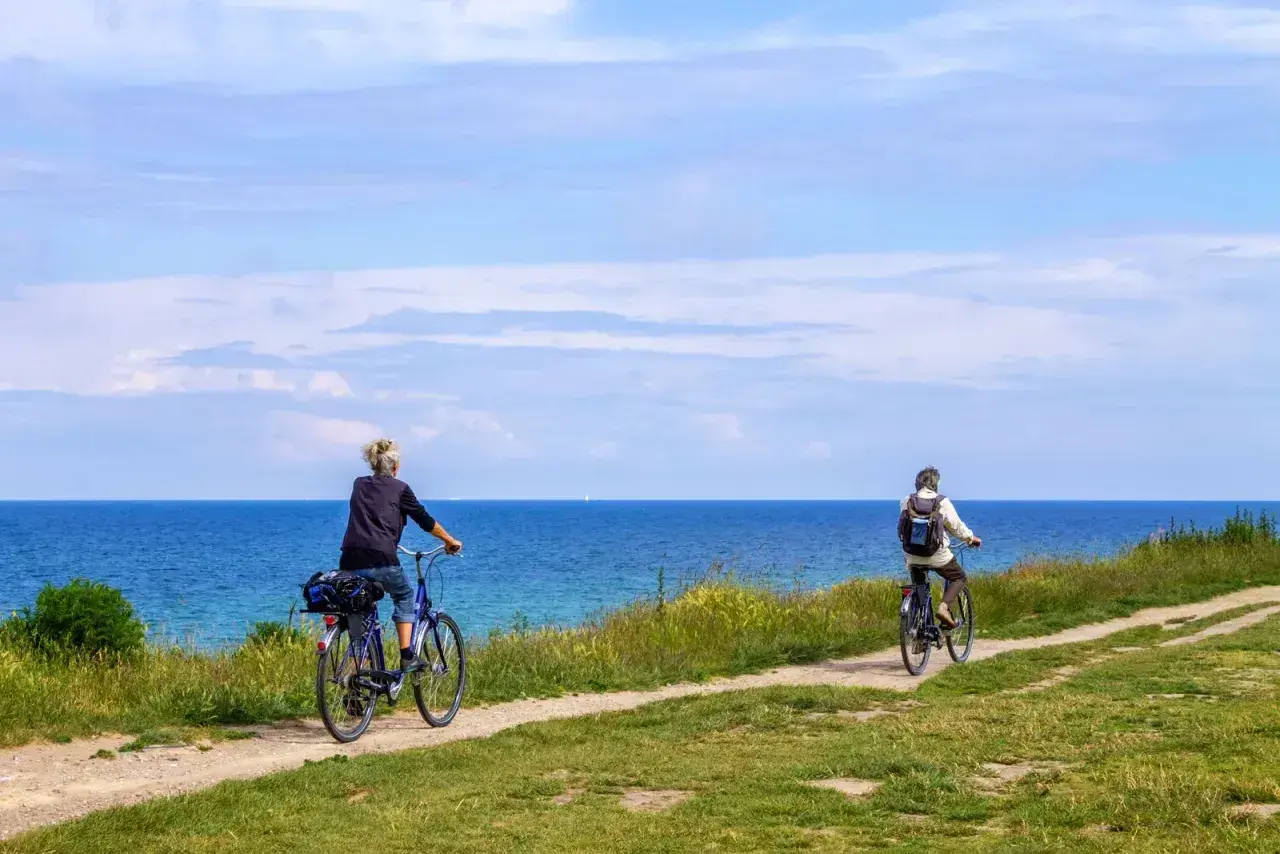 Dwie osoby na rowerach przemierzają malowniczą trasę rowerową R10 wzdłuż błękitnego morza.