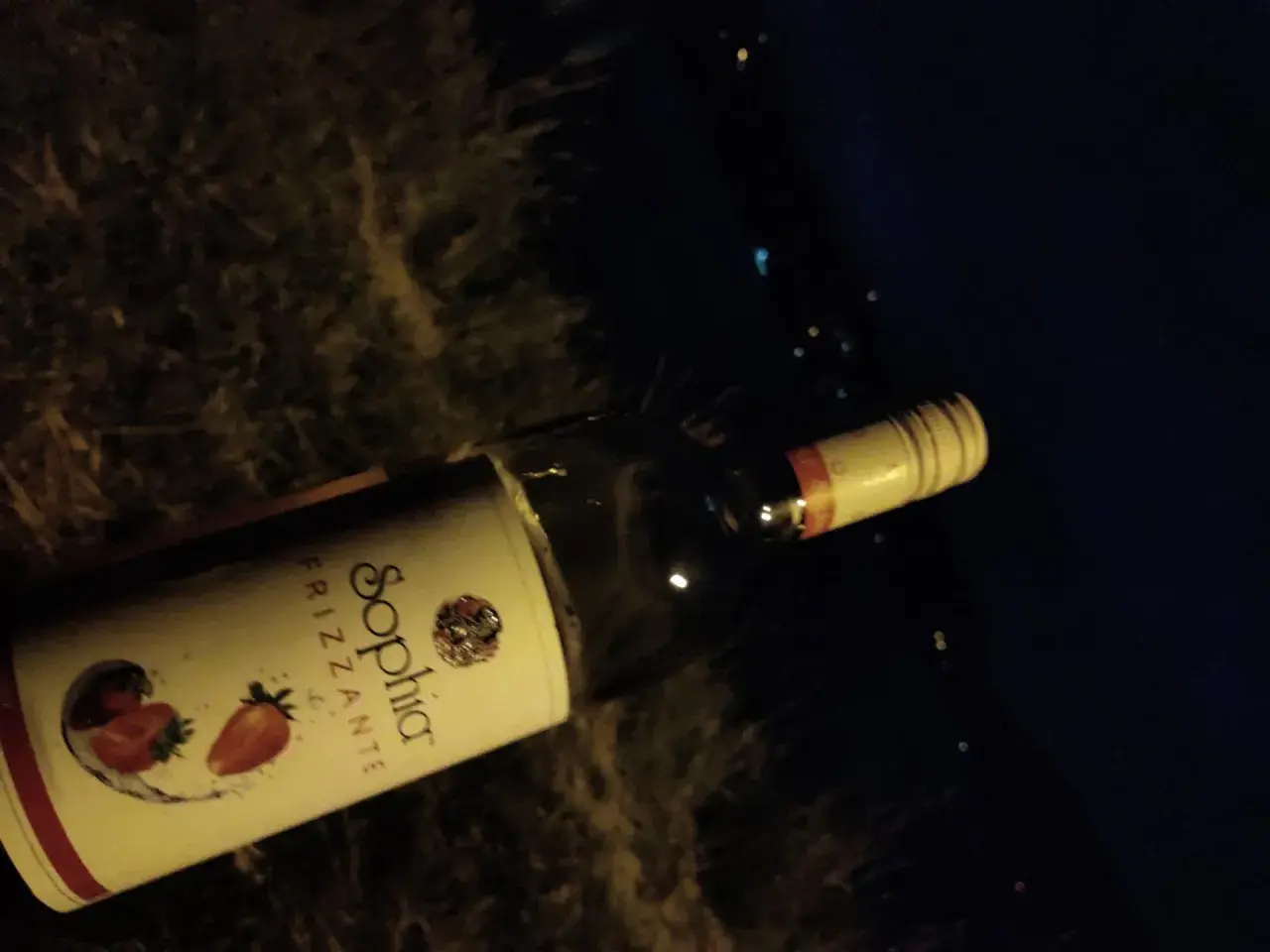 Butelka wina Sophia Frizzante z truskawkami na etykiecie, leżąca na ciemnym tle.