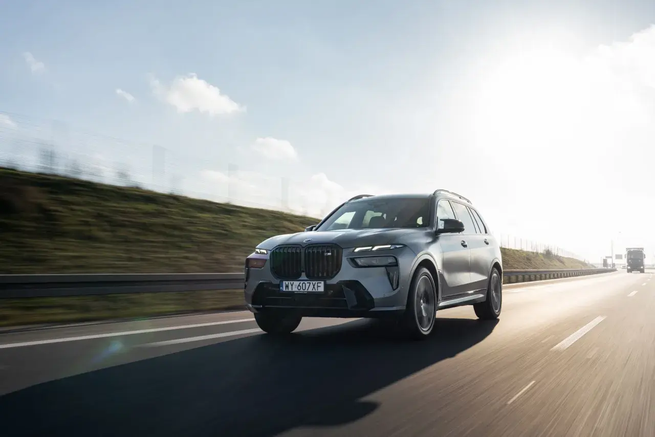 Szary BMW X7 M60i pędzi autostradą w słoneczny dzień.