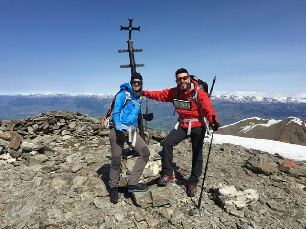 Dos montañistas celebran en la cima del Fontalba Puigmal, con un cruce metálico y vistas nevadas.