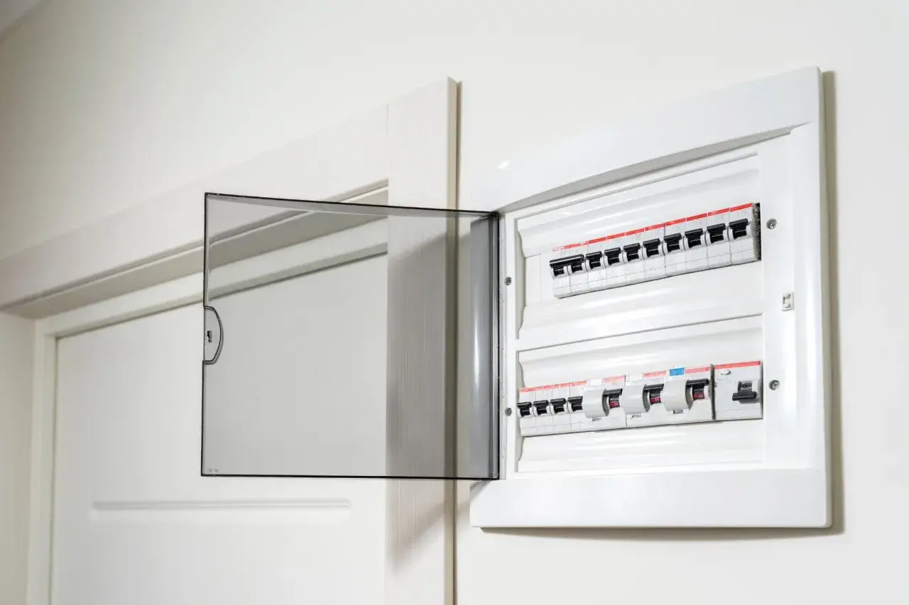 Otwarta biała skrzynka z bezpiecznikami elektrycznymi na ścianie.