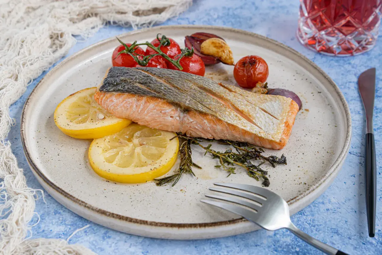 Gebratener Lachs mit Haut, serviert mit Zitronenscheiben, Kirschtomaten und Kräutern. Ein köstliches Rezept für Lachs mit Haut.