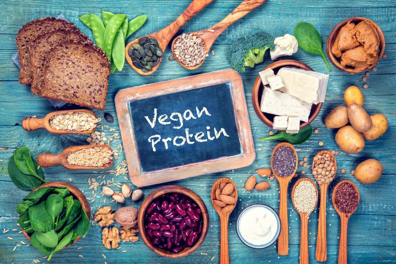 Na stole pełnym roślinnych produktów: chleb, fasola, orzechy, nasiona, tofu, warzywa i jogurt. To dowód, że wegańskie białko jest łatwo dostępne i smaczne.