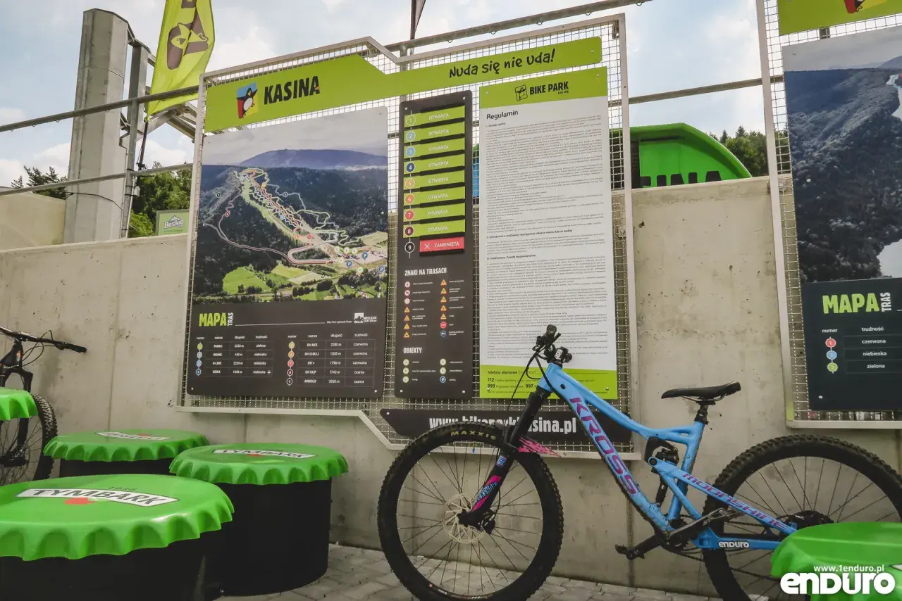 Mapa tras w bike parku Kasina z regulaminem i oznaczeniami trudności. Obok stoi rower enduro.