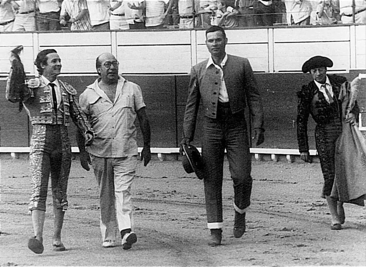 Un sayalero y un bandrés caminan juntos en la arena. El sayalero, con traje de luces, saluda.