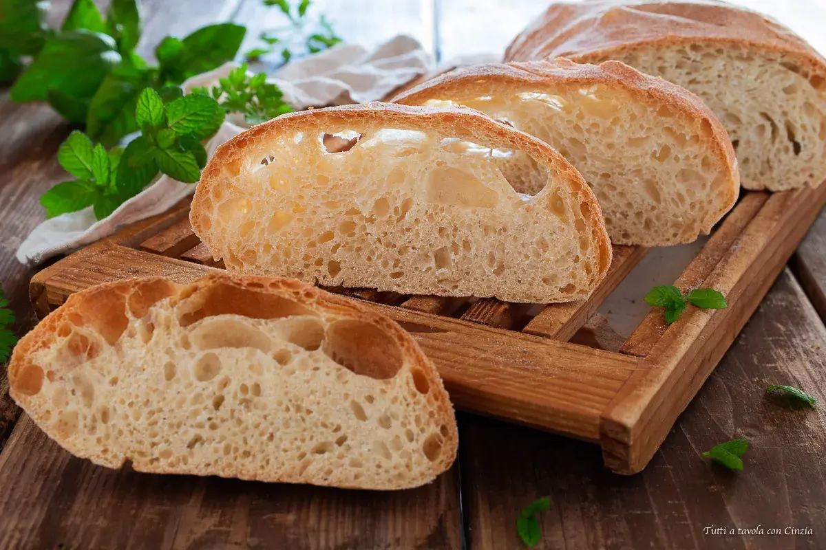 Fette di pane soffice con alveolatura pronunciata, su un tagliere di legno, con foglie di menta fresca.
