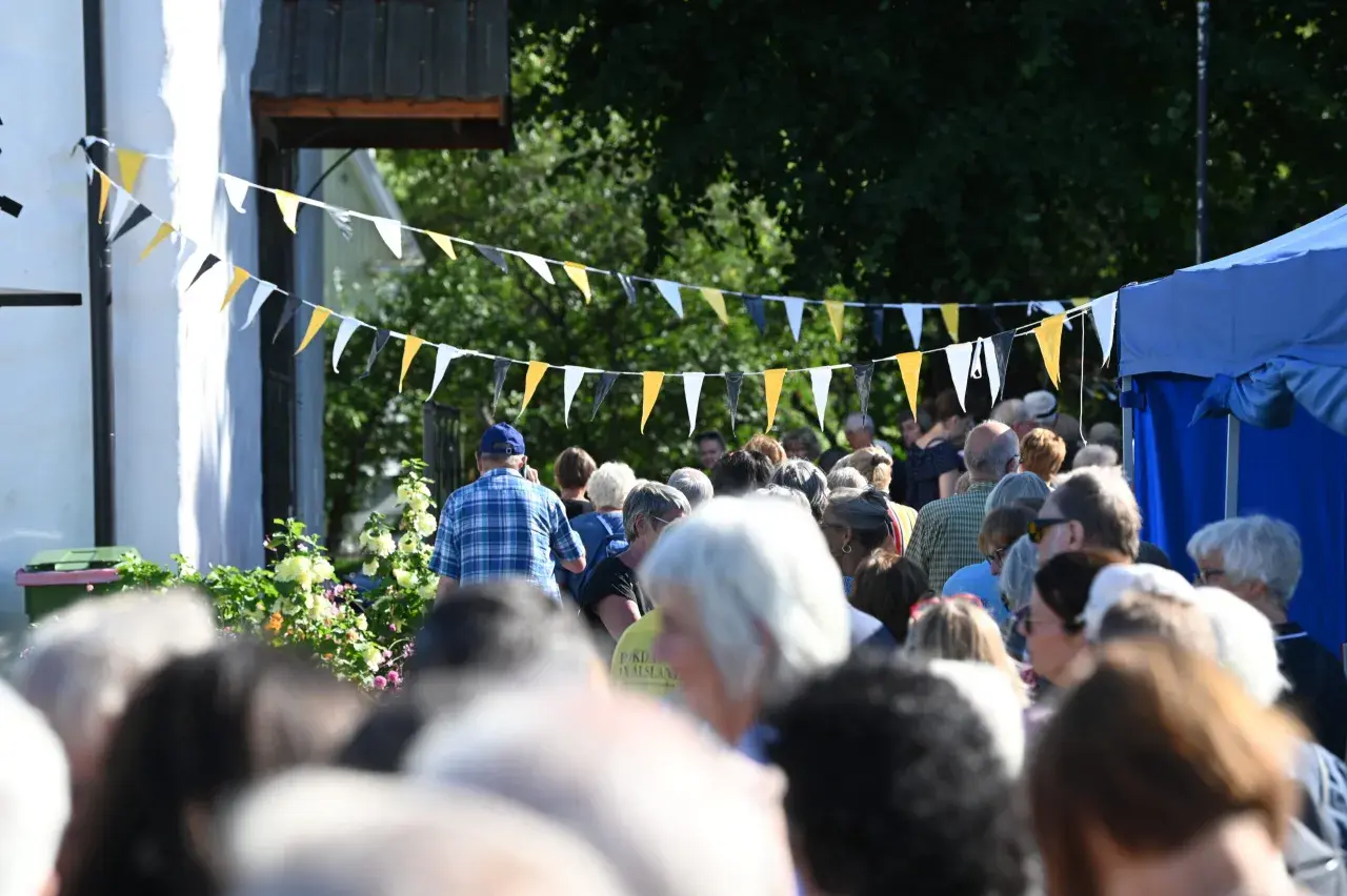 Folk samlas under flaggspel vid bokdagar i Dalsland. En man i rutig skjorta går framåt.