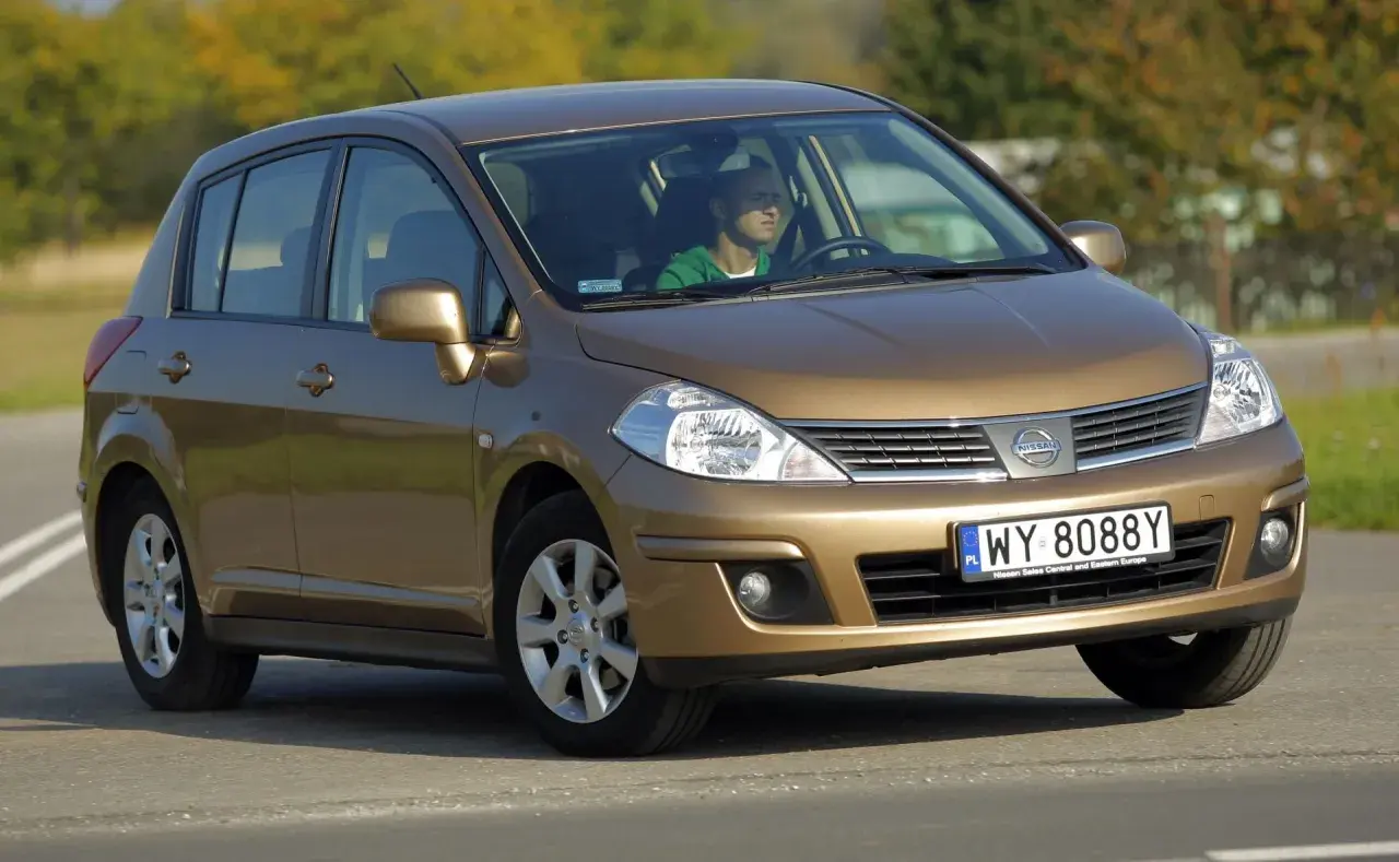 Złoty Nissan Tiida z mężczyzną za kierownicą jedzie po drodze.