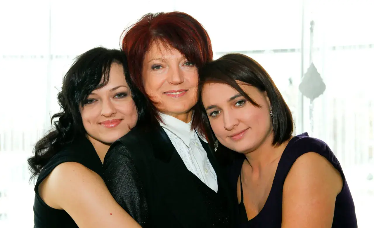 Trzy kobiety: starsza z rudymi włosami w czarnej marynarce i dwie młodsze, córki, obejmujące ją.