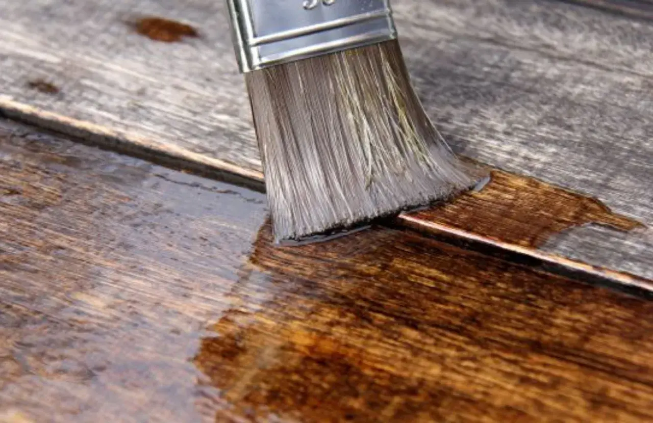 Pennello stende olio paglierino per legno su assi grezze, nutrendo e proteggendo la superficie.