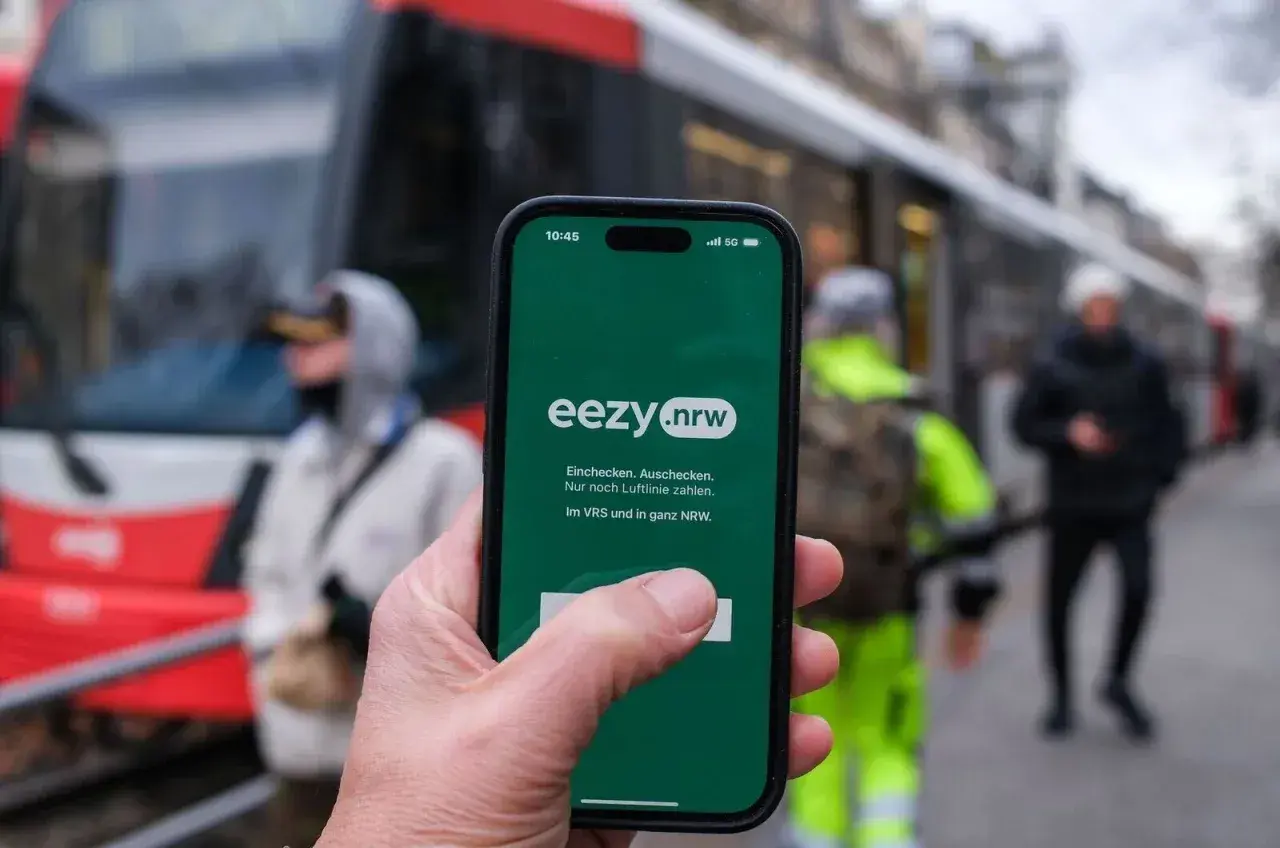 Hand hält Smartphone mit eezy.nrw App. Einfach einchecken, auschecken und nur nach Luftlinie zahlen in Westfalen.