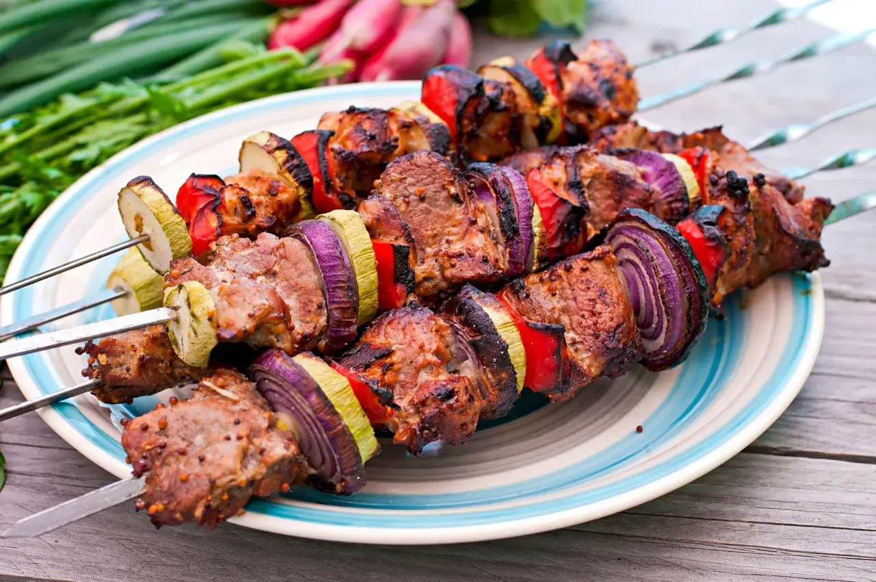 Brochettes d'agneau grillées avec oignons rouges, poivrons et courgettes sur une assiette, prêtes à être dégustées.