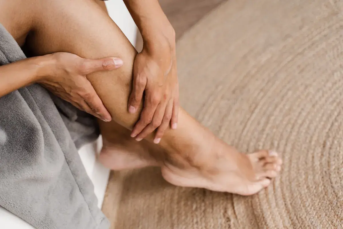 Mani che massaggiano un polpaccio, alleviando la sensazione di gambe che bruciano su un tappeto di iuta.