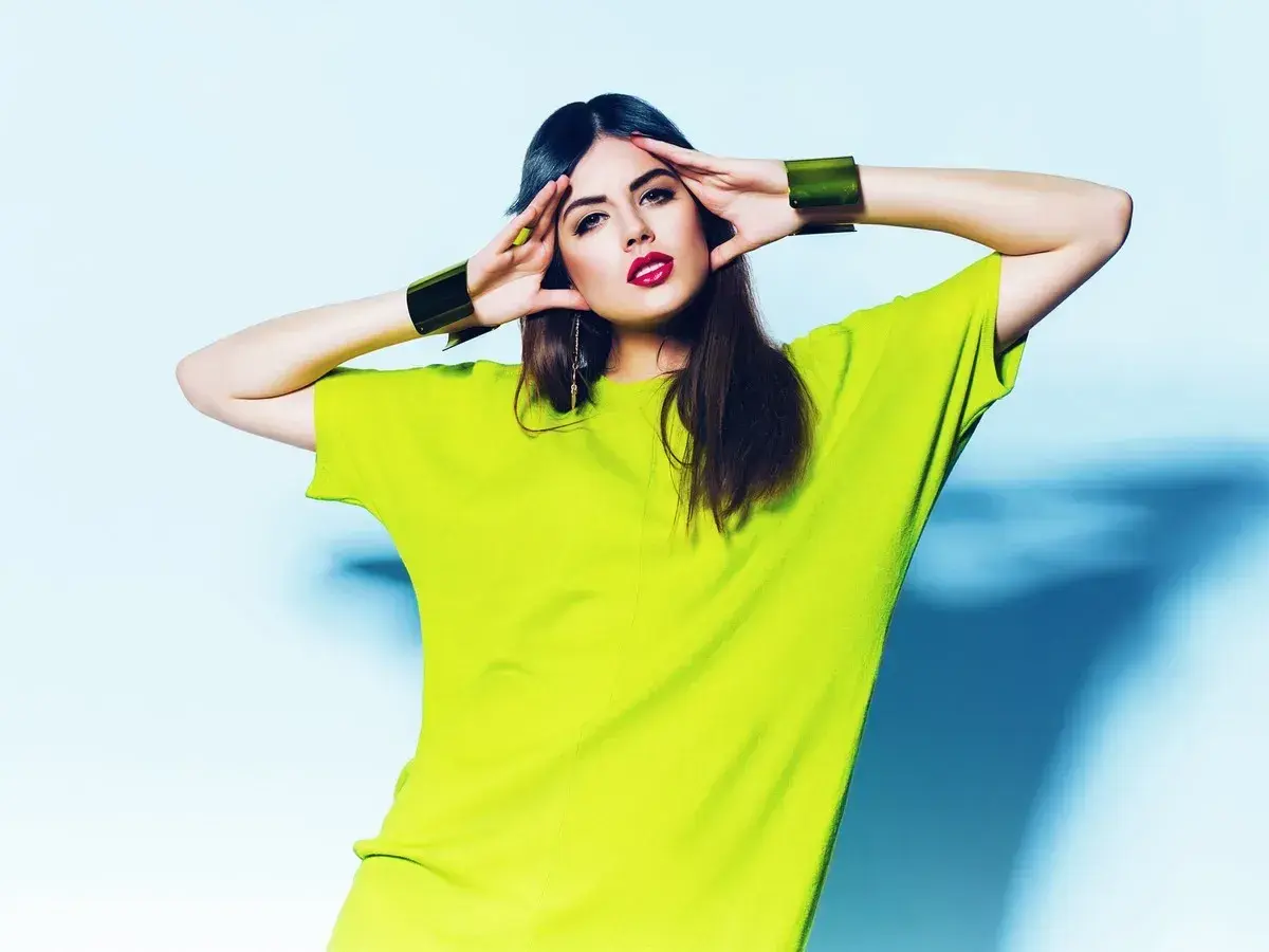 Modelka w limonkowym, luźnym T-shircie i złotych bransoletach, prezentująca najnowszy trend.