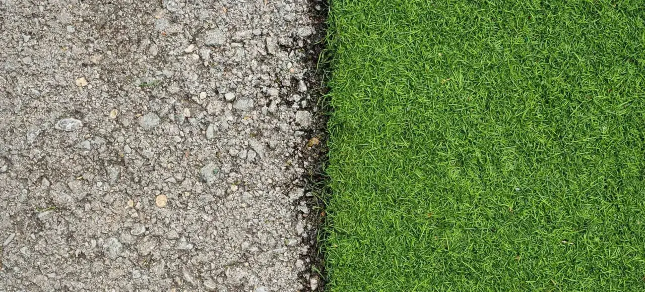 Superficie de asfalto gris y césped natural verde vibrante, mostrando la transición de poner césped artificial sobre césped natural.