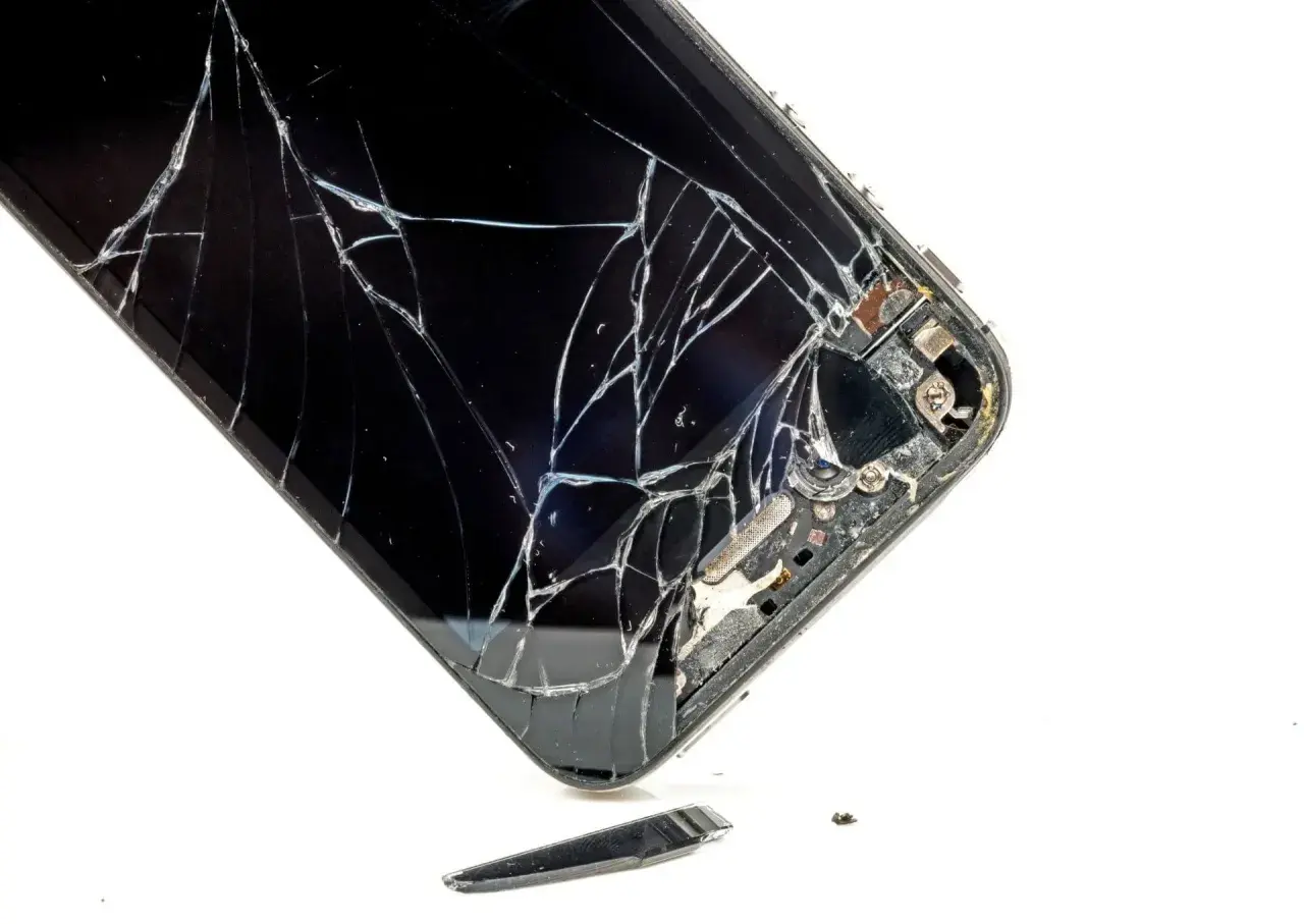 Rozbite szkło telefonu. Widać pęknięcia i fragmenty, które odpadły. To pokazuje, czym się różni szkło hartowane od hybrydowego w praktyce.