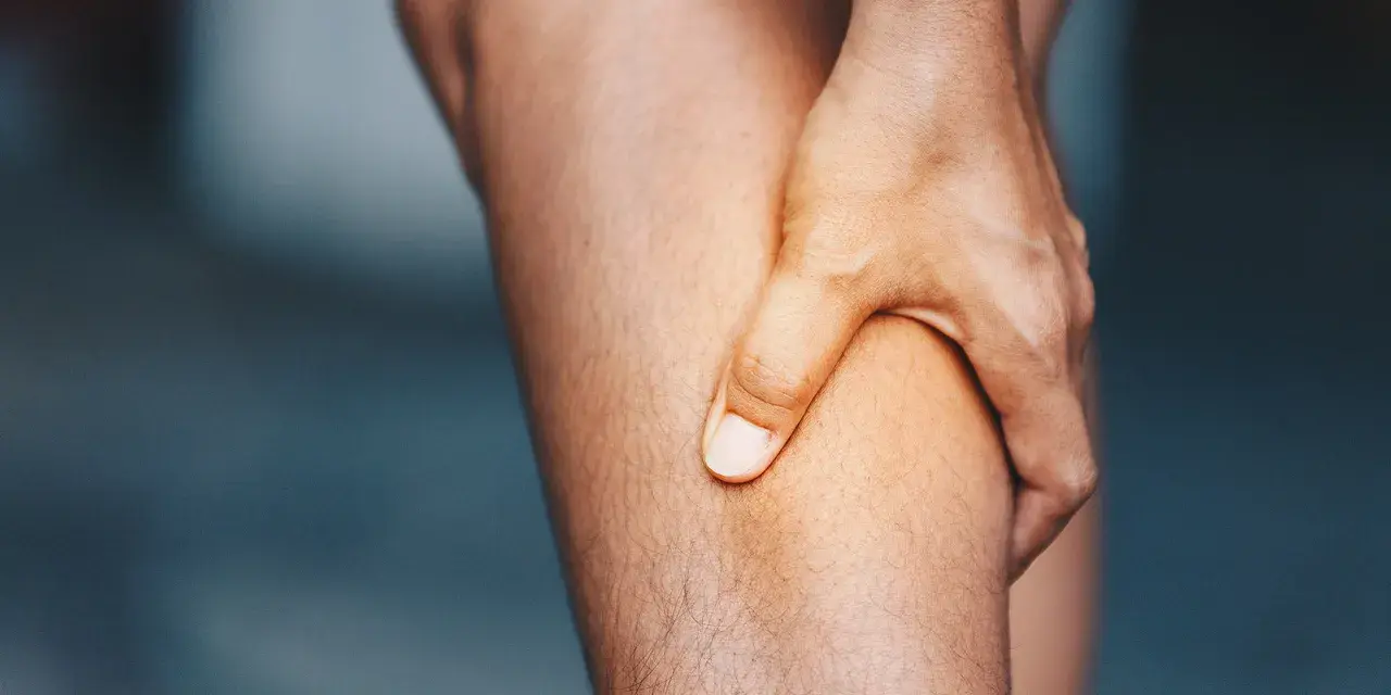 Hand greift an schmerzendes Bein. Was hilft gegen Muskelschmerzen?