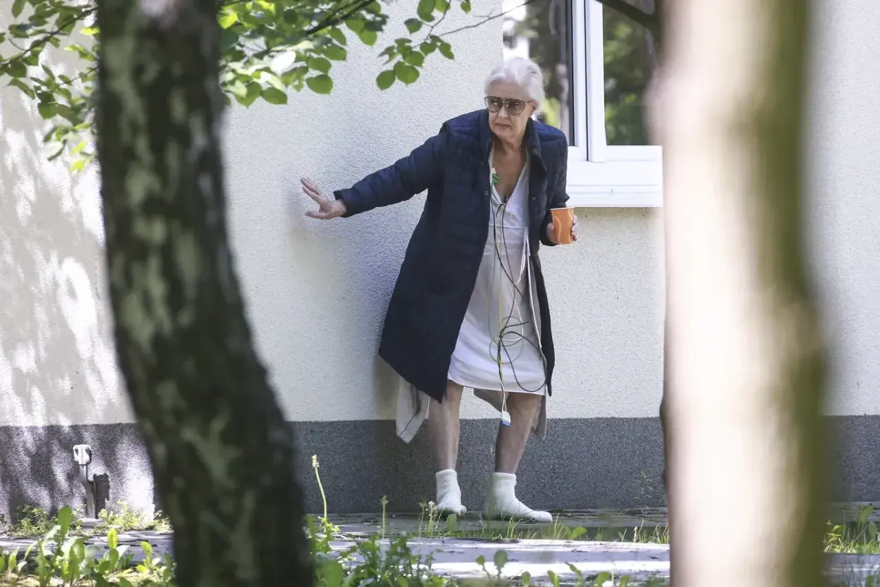 Beata Tyszkiewicz w domu opieki, z kubkiem w dłoni, oparta o ścianę.