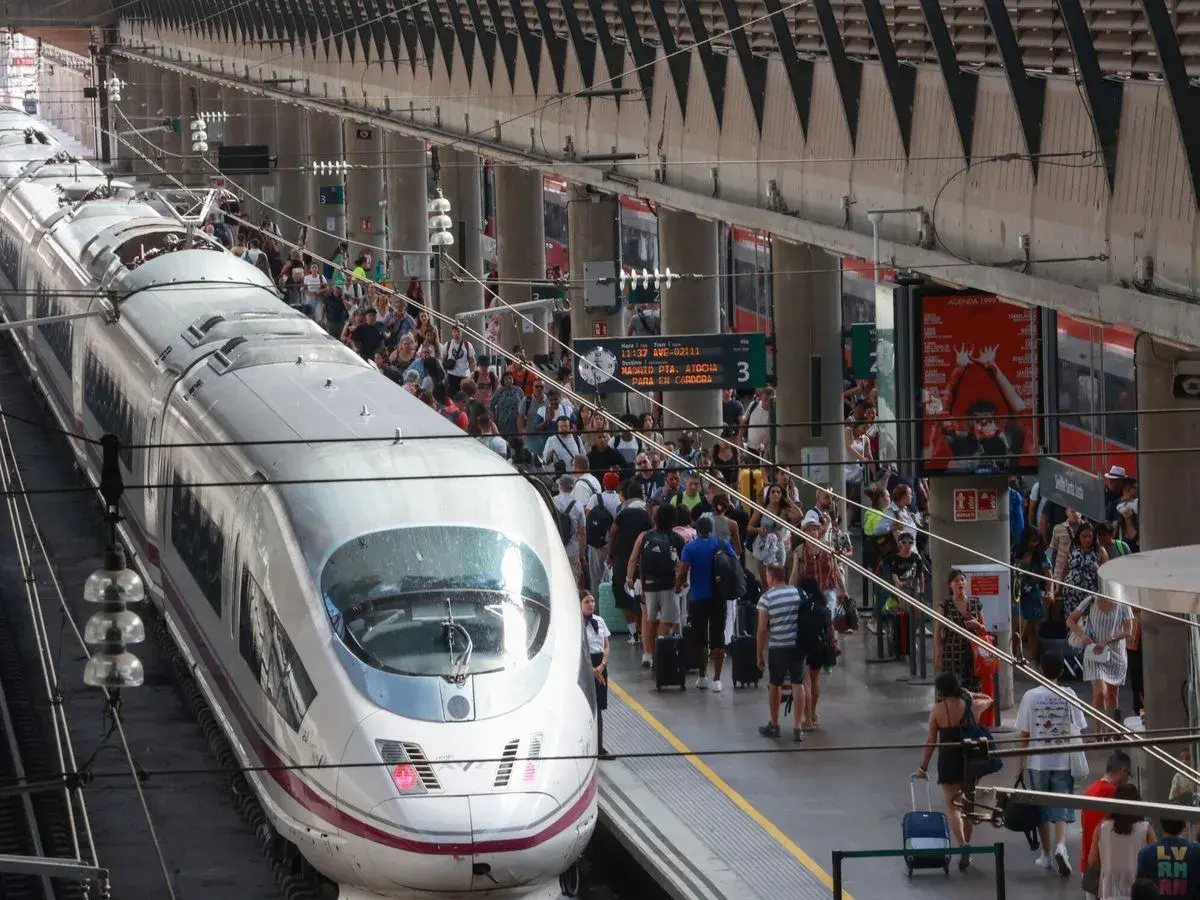 Un tren AVE espera en la estación, listo para llevar pasajeros de Lleida a Sevilla. Gente con maletas se agolpa en el andén.