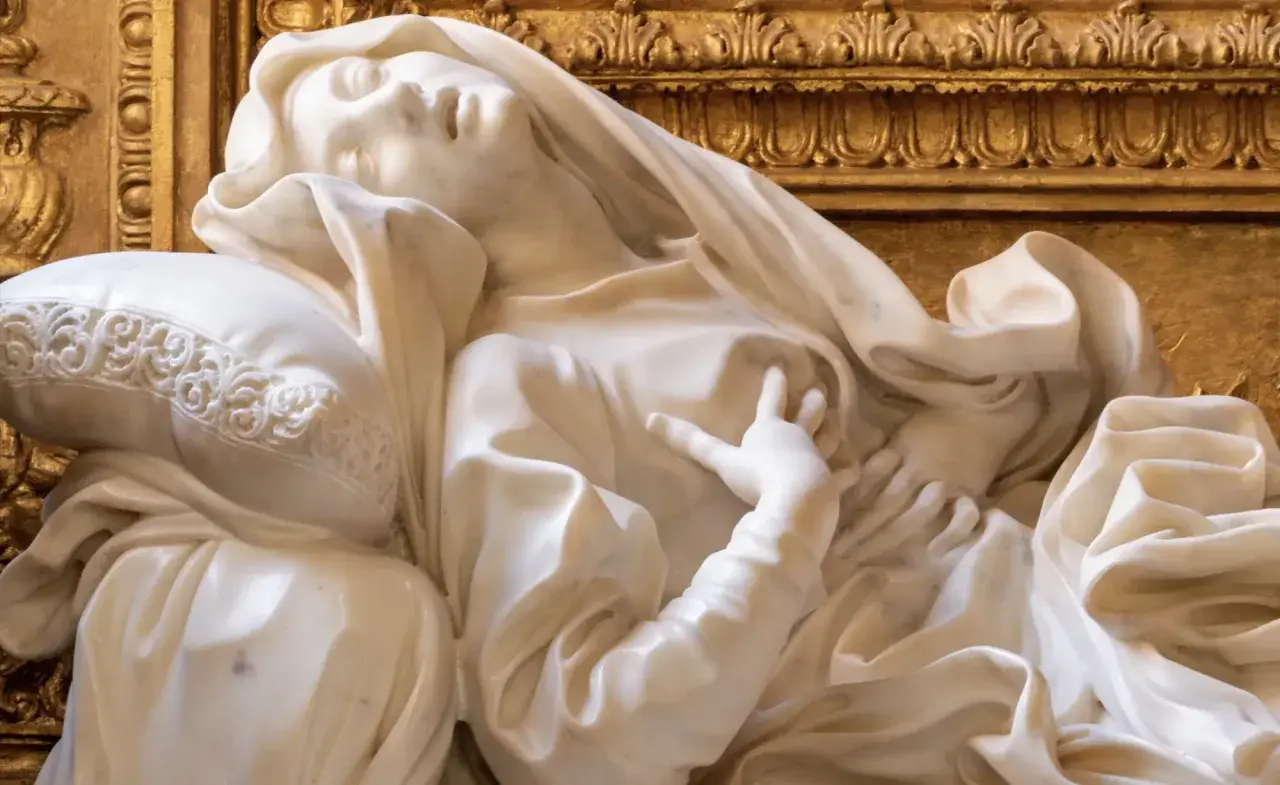 Estasi di Santa Teresa a Roma, marmo bianco su fondo dorato. La santa giace su un cuscino, con un'espressione di profonda emozione.