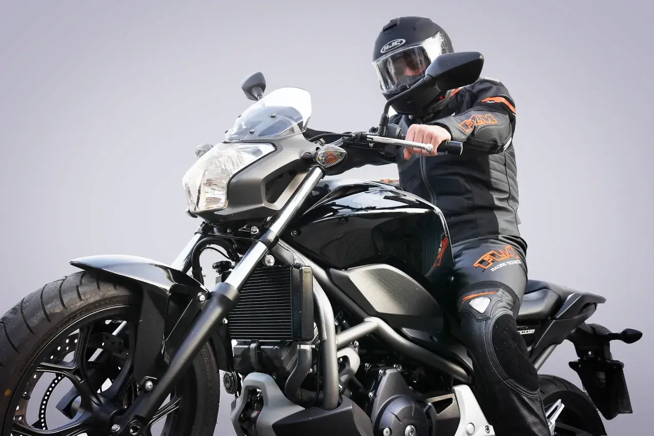 Motocykl od ilu lat? Młody motocyklista w czarnym kombinezonie i kasku na czarnym motocyklu.
